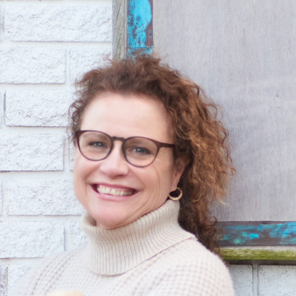 head shot of Eileen Duffy, she has long curly hair and is wearing round glasses and an ecru turtle next sweater