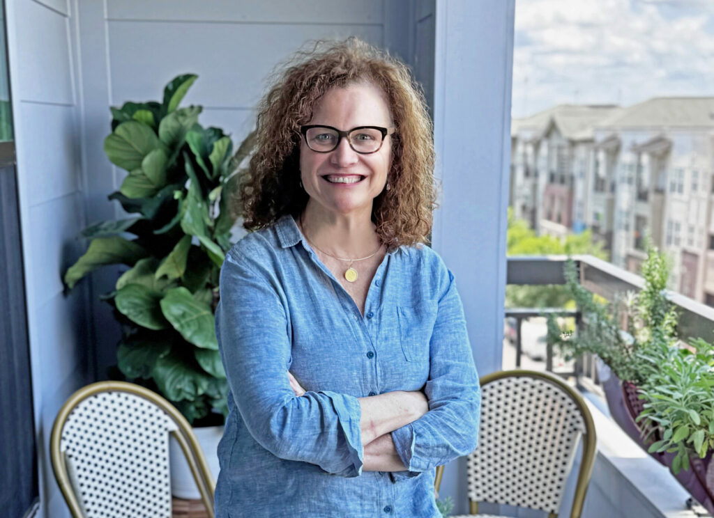 Eileen Duffy stands on a balcony with her arms crossed. Wearing a blue shirt, she is posing for a portrait.