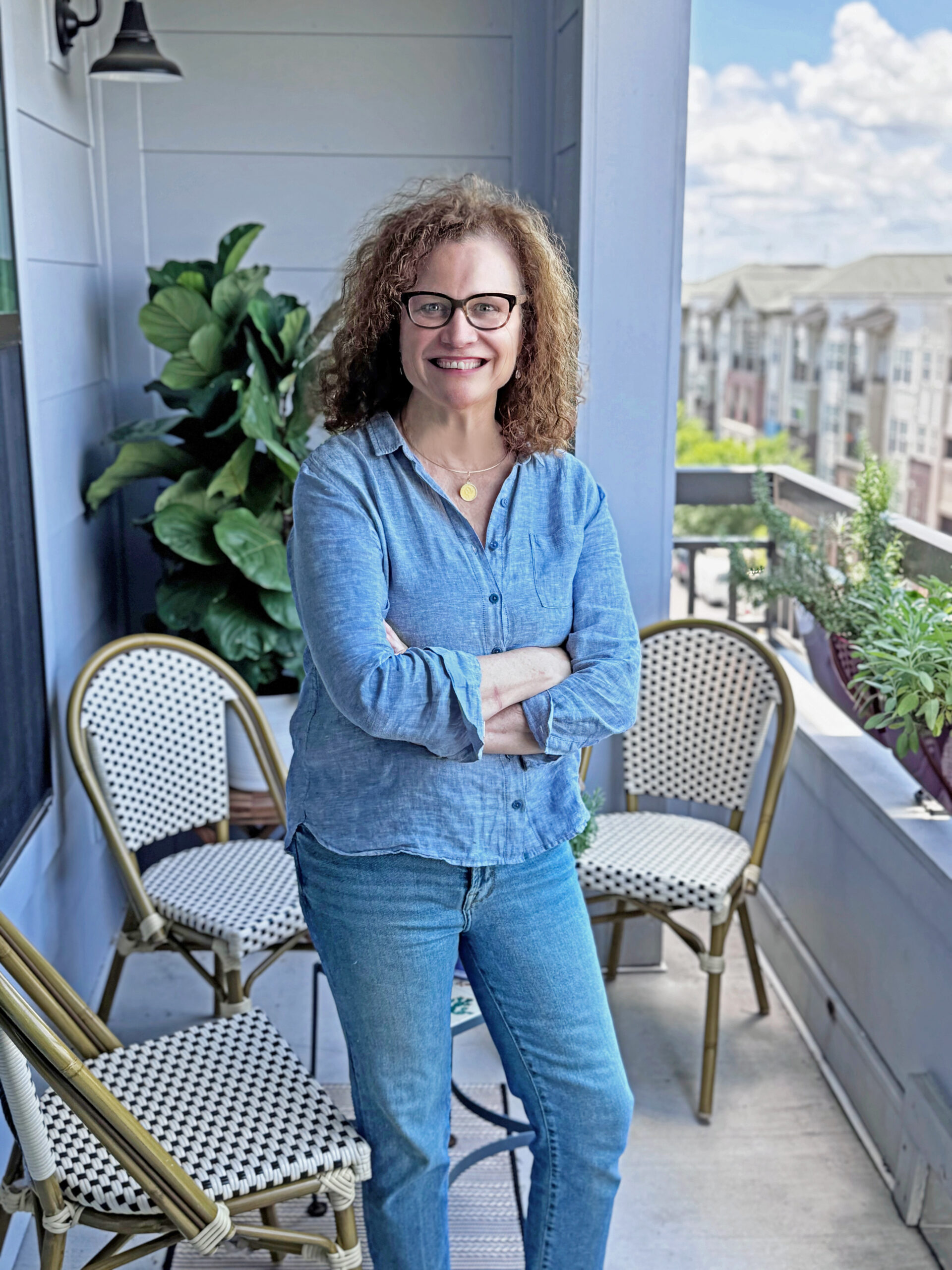 Eileen Duffy stands on a balcony with her arms crossed. Wearing a blue shirt, she is posing for a portrait.