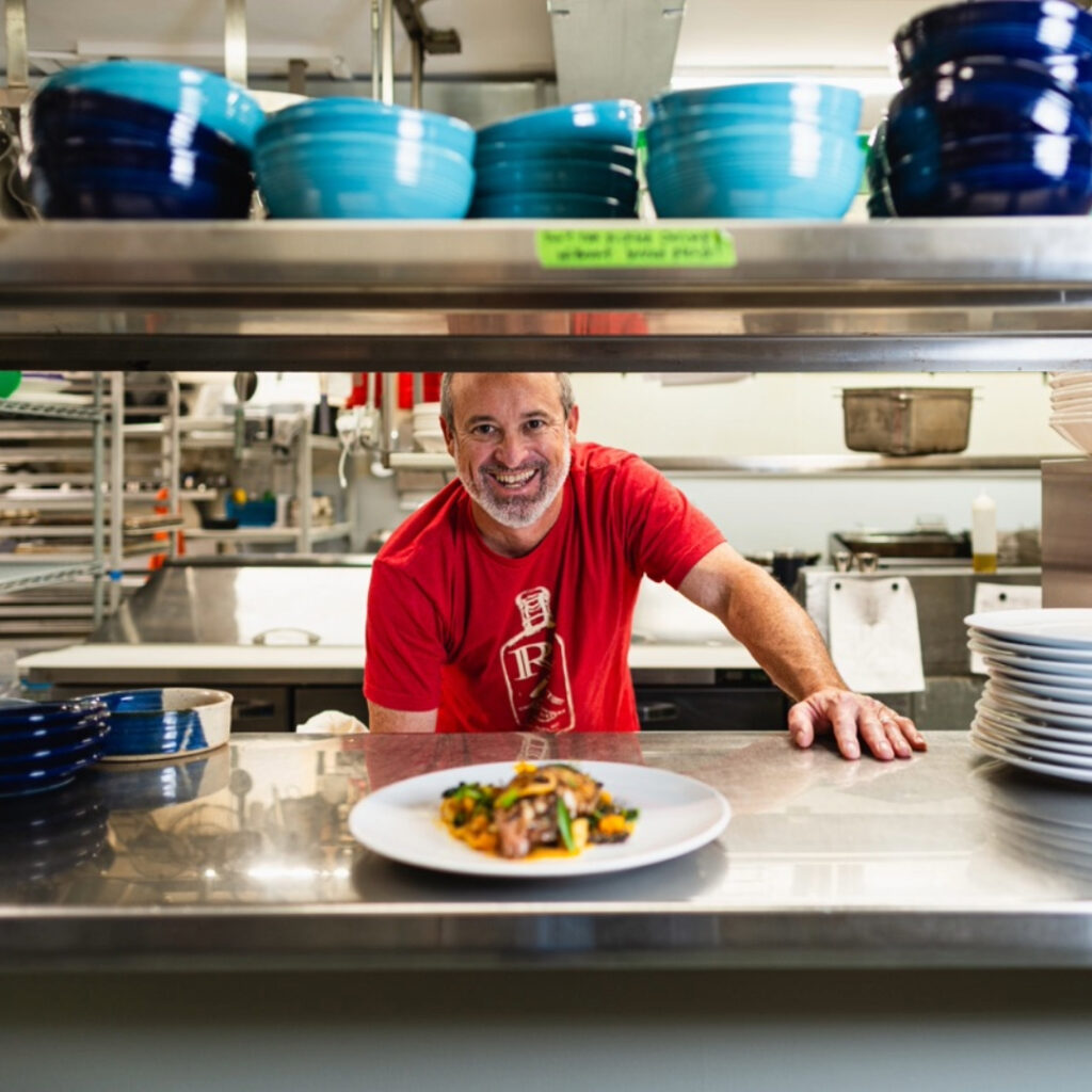 chef in red shirt behind the line, pushes a plate towards you.