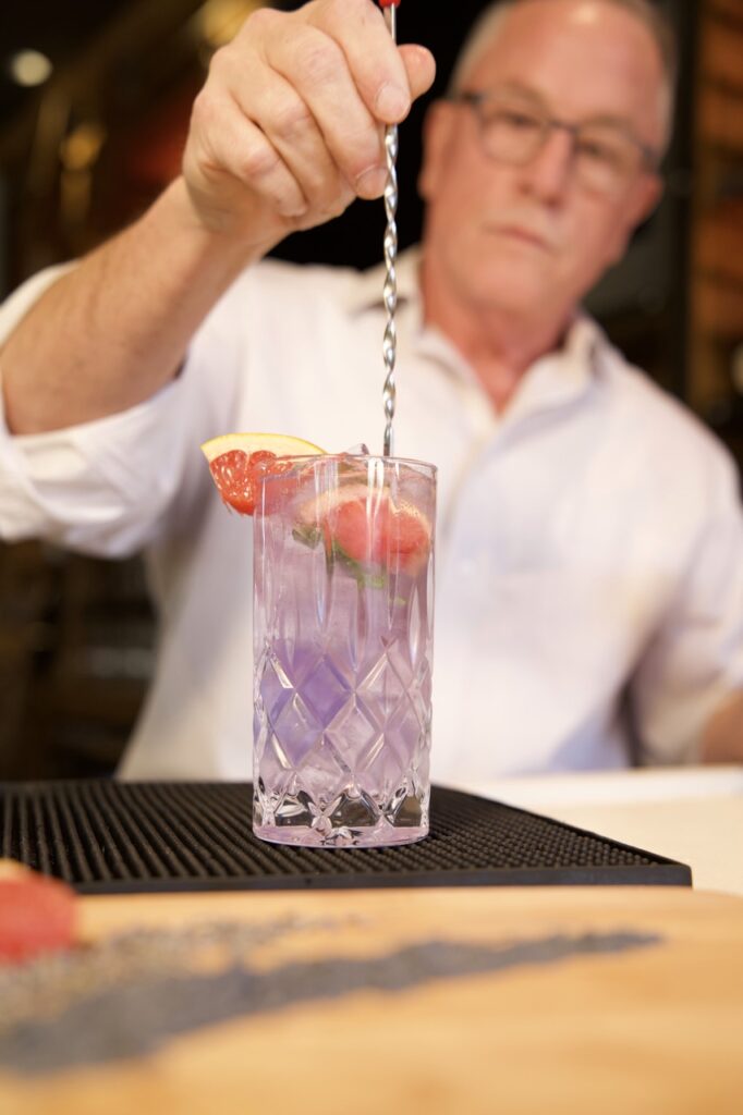 man stiring a purple cocktail with grapefruit slices