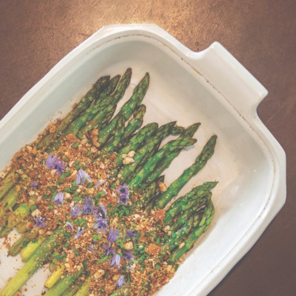 asparagus in a white dish with bread crumbs and purple chive flowers
